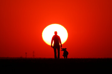 Woman walks with her dog at sunset.