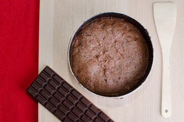 Wooden base with brownie in the mold, wooden spatula and chocolate.
