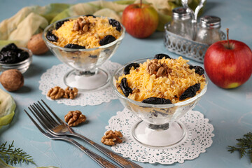 Two servings of salad with chicken, cheese and apples, decorated prunes and walnuts in glasses bowls on light blue background