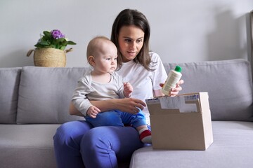 Young mother with baby in her arms unpacking parcel with online shopping