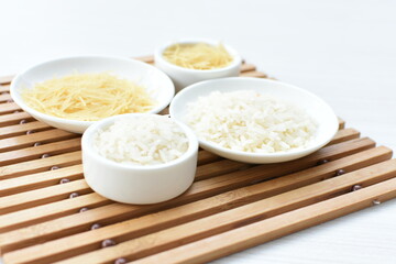 Short pasta spaghetti angel hair and uncooked rice displayed in containers on white background