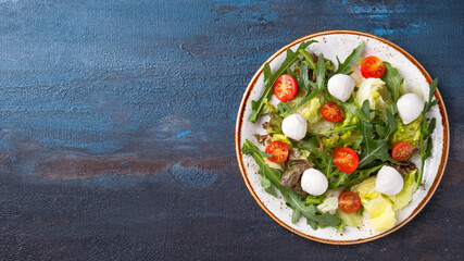 Diet salad with arugula, fresh vegetables and cheese on a plate. Top view, text space