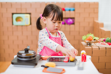 toddler girl pretend play food preparing role against cardboard blocks kitchen background