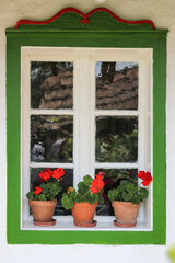 Traditional country house's old window. In the window there are red geranium flowers (Pelargonium zonale) in flowerpots. Farmhouse window with red flowers. Europe Hungary.
