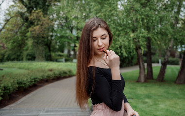 Stylish girl paints her lips with lipstick on a walk. Cute young girl applies makeup in the park.