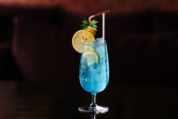 Cocktail Blue Lagoon close-up on a bar with a slice of lemon, stylish decor and a straw. Ice cubes in a cocktail, bubbles. Side view