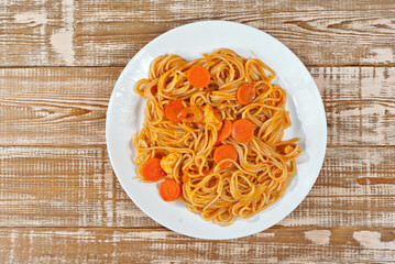 Pasta with carrots in a white plate on a wooden table. Vermicelli with orange sauce on a pink shabby board. Place for text near the plate. Copy space for design.