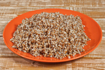 Buckwheat in a green plate on a wooden table. Food in utensils on the background of an old pink shabby board.