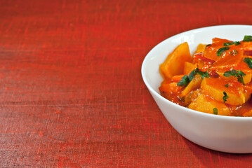Potatoes in a white plate on a wooden table. Boiled potatoes with orange sauce on a red board. Place for text near the plate. Copy space for design.