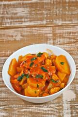 Potatoes in a white bowl on a wooden table. Boiled potatoes with orange sauce on a pink shabby board. Place for text near the plate. Copy space for design.