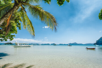 El Nido, Palawan island, Philippines. Palm trees of Corong Corong beach, island hopping boats in blue shallow lagoon and blue sky