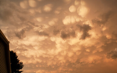 Ominous clouds appear before a thunderstorm with an eerie yellow gold color, with a home or building with a. tree on the extreme left.