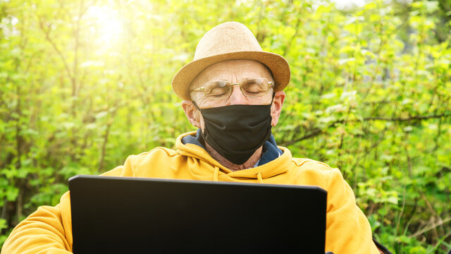 senior man in mask glasses falls asleep at laptop in garden