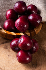 Some plums in a basket with jute fabric. Wood background