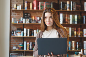 Dreamy girl holding laptop and looking away in cafe