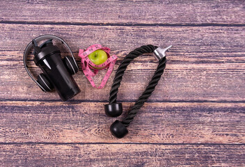 Gym equipment on wood background: water bottle, cellphone, green apple, headphones. Space for text. Copy space
