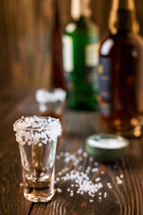 An empty tequila glass, with salt at the edges, stands on the bar, in the background are different bottles of alcohol, shallow depth of field, selective focus. The concept of a drink in the bar.