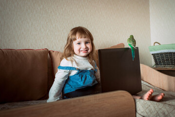 Beautiful little girl sitting on couch in living room and using laptop computer.Online training, games and watching cartoons. New generation. bright room.