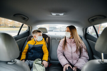 A mother with a child in the back seat of a car in masks going to the hospital. Epidemic, quarantine