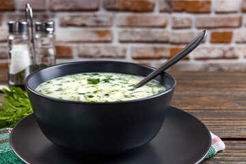 Cold soup with fresh cucumbers, radishes with yogurt in a bowl on wooden background. Traditional Russian food - okroshka. Vegetarian food. Healthy eating concept.