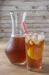 Iced tea with straw, ice cubes and sliced lemon over wooden background