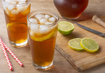 Iced tea with straw, ice cubes and sliced lemon over wooden background