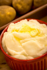 Mashed Potatos in red ramekin with butter with potatos in the background