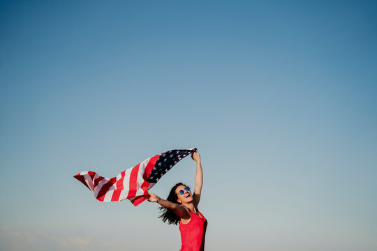 young woman holding United States flag outdoors at sunset. Independence day in America, 4th July concept - Powered by Adobe