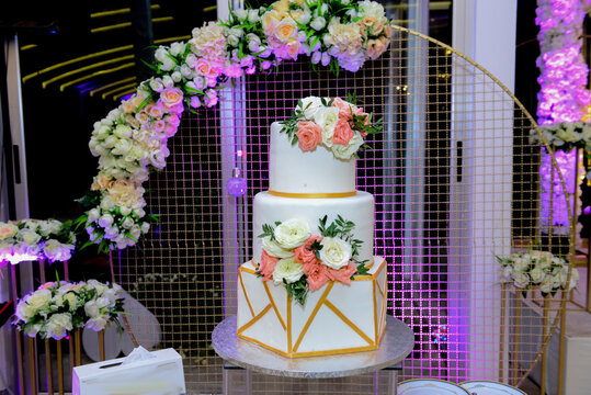 A multi level white wedding cake on a silver base and pink flowers on top