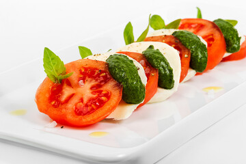 Tomato and mozzarella slices decorated with basil leaves on a plate and white background. As backdrop for menus, cookbooks, advertisements and other culinary projects