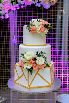 A multi level white wedding cake on a silver base and pink flowers on top