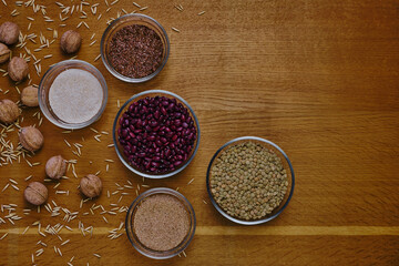 Top view of walnuts, seed, flax, beans, lentils and bran set in glass bowls as healthy dietary food on wooden board. Creative flatlay with cererals.