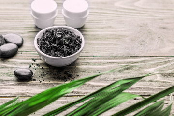 Spa still life.Spa - composition with stones and black sea salt on a wooden table in the sunlight. Green leaves in the foreground. Copy space.