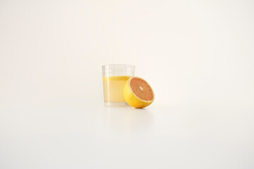 Front shot of a glass cup filled with organic grapefruit juice and half organic grapefruit on a white background. Copy Space