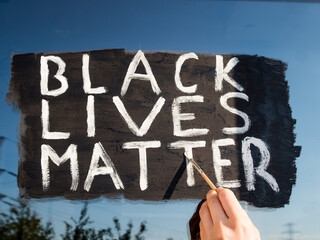 Young white girl painting Black Lives Matter text on glass window. Sign against racism, for human...