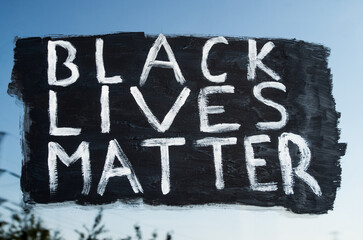 Young white girl painting Black Lives Matter text on glass window. Sign against racism, for human rights and freedom of all people
