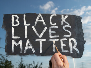 Young white girl painting Black Lives Matter text on glass window. Sign against racism, for human rights and freedom.