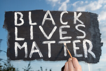 Young white girl painting Black Lives Matter text on glass window. Sign against racism, for human rights and freedom.