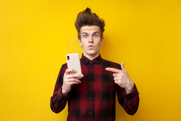 shocked guy with funny hairstyle use smartphone on yellow isolated background, hipster holds phone and is surprised