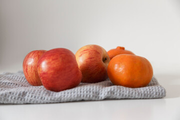 Front shot of organic apples and tangerines over a gray kitchen towel on a white table