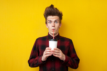 shocked guy drinks energy coffee on a yellow isolated background, a man with a funny hairstyle...