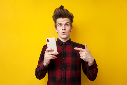 shocked guy with funny hairstyle use smartphone on yellow isolated background, hipster holds phone and is surprised