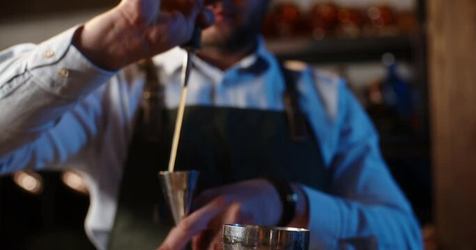 Professional bartender masterly creating a cocktail in modern bar. Experienced barman adding syrip into shaker using jigger - food and drink, nightlife close up 4k footage