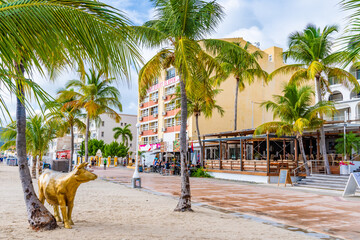 Philipsburg, Sint Maarten. Holland House Beach Hotel golden cow on sand below coconut palm trees by...
