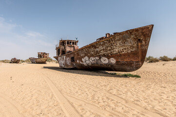 Fototapeta na wymiar Moynaq, Uzbekistan 09 20 2019: Rusting shipwrecks on Aral Desert in former area of Aral sea harbor in village of Mo'ynaq, evidence of ecological cathastrophy
