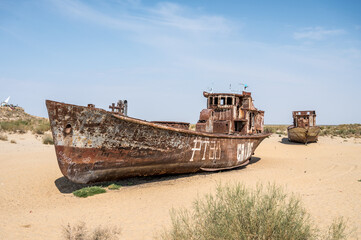 Fototapeta na wymiar Moynaq, Uzbekistan 09 20 2019: Rusting shipwrecks on Aral Desert in former area of Aral sea harbor in village of Mo'ynaq, evidence of ecological cathastrophy