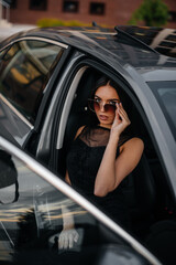 Stylish young girl sitting in a business class car in a black dress. Business fashion and style