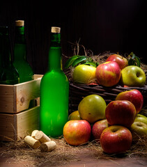 Asturian cider bottles wooden crate with many red and green apples at wicker basket over wooden...