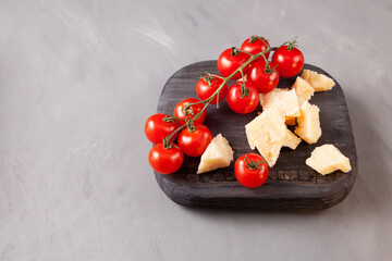 Small red cherry tomatoes and slices of cheese on an old wooden board, closeup. Gray background, copy space