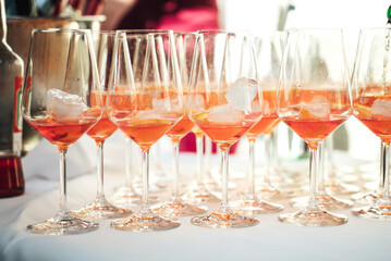 Rows of glasses with orange drink and ice cubes standing on buffet table. Alcoholic beverage....